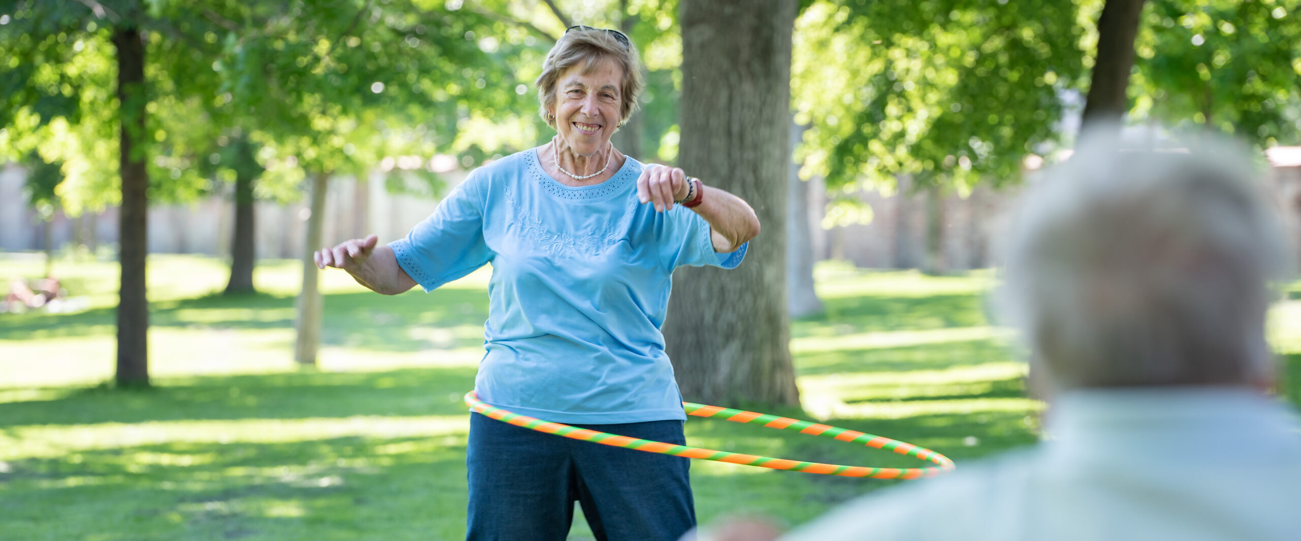 Eine Seniorin tanzt mit einem Hula Hoop Reifen im Augarten.