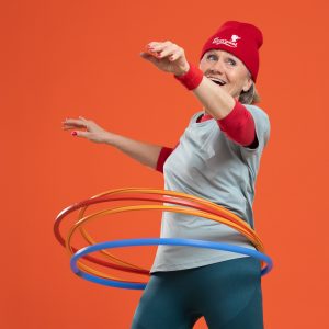 ChatGPT: Eine fröhliche ältere Dame mit sportlicher Kleidung tanzt mit mehreren bunten Hula-Hoop-Reifen.