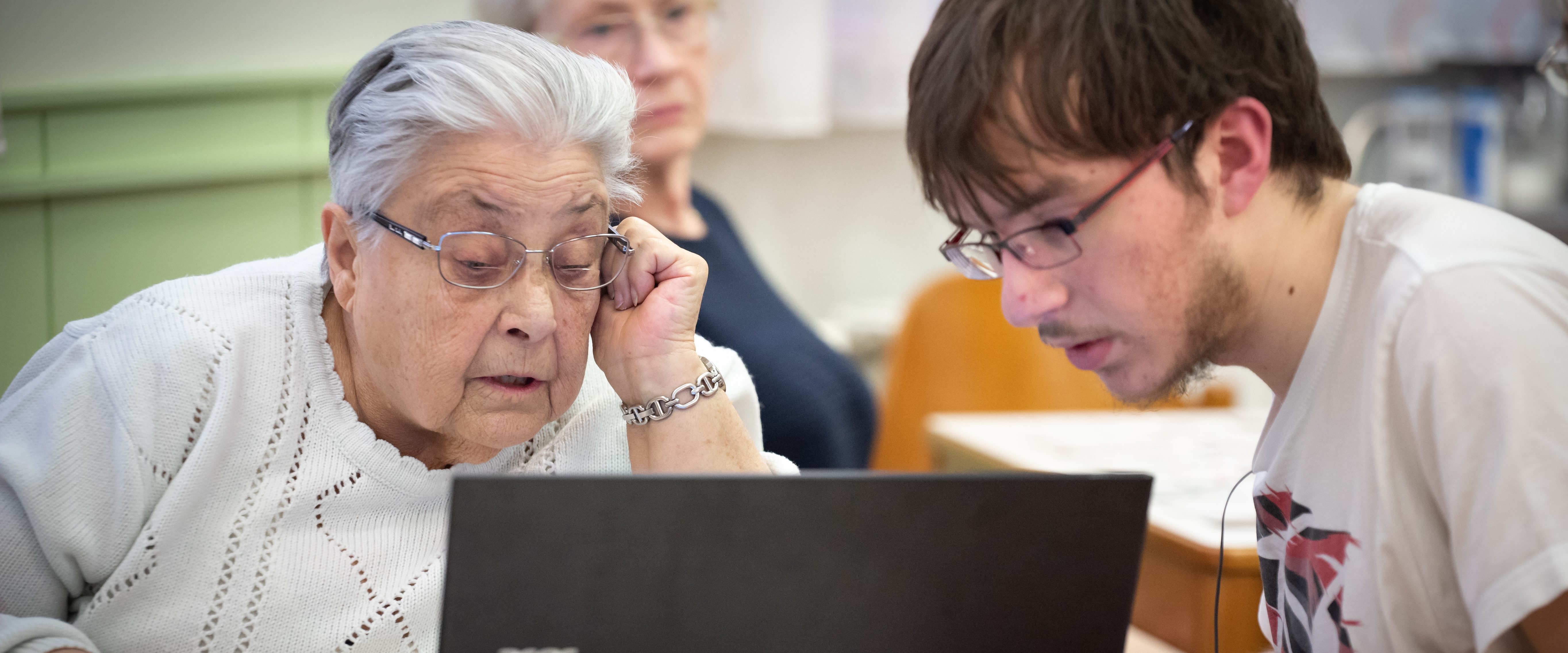 Seniorin und Jugendlicher schauen gemeinsam auf Laptop-Bildschirm