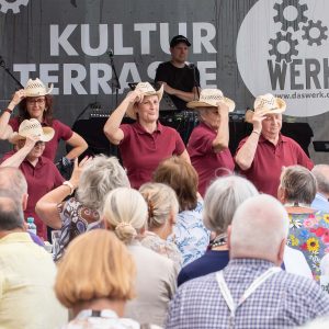 Freiluftbühne Das Werk Wien am Donaukanal. Eine Line Dance Gruppe tanzt vor begeistertem Publikum.