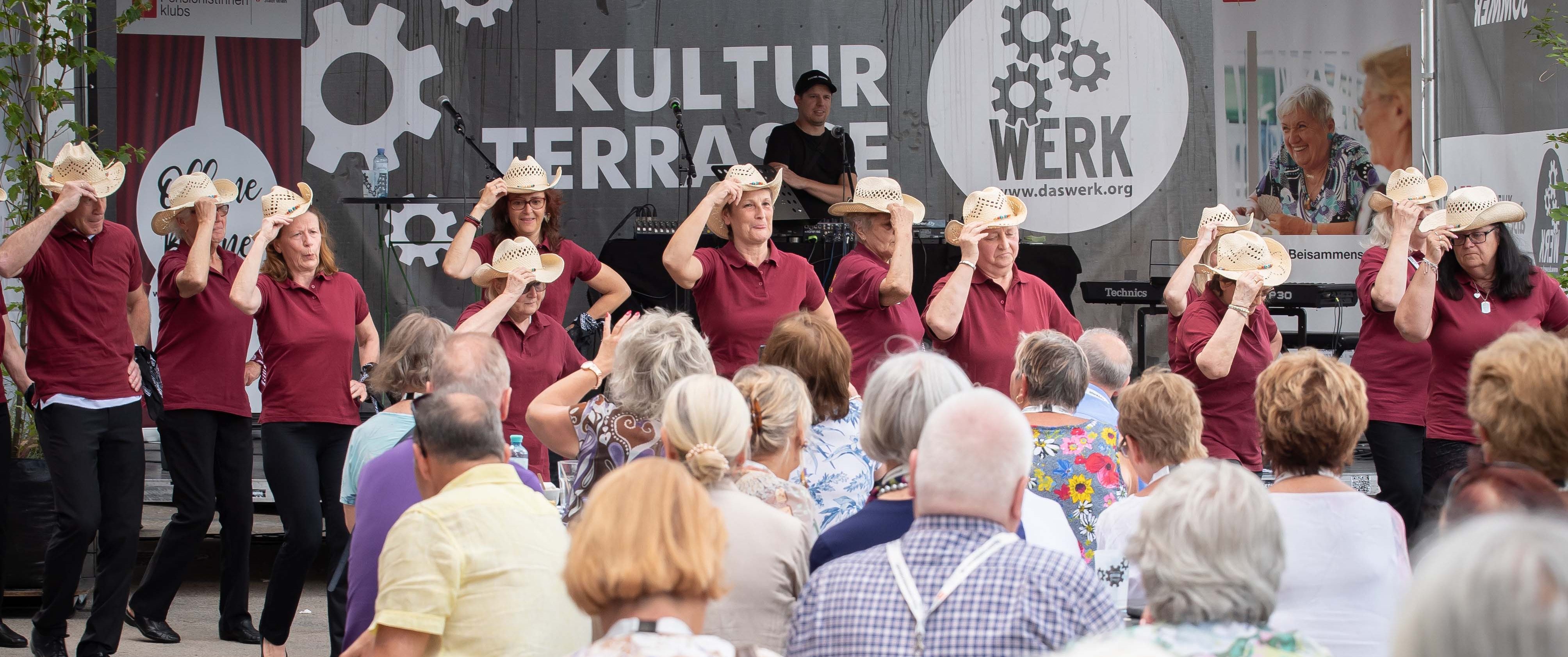 Freiluftbühne Das Werk Wien am Donaukanal. Eine Line Dance Gruppe tanzt vor begeistertem Publikum.