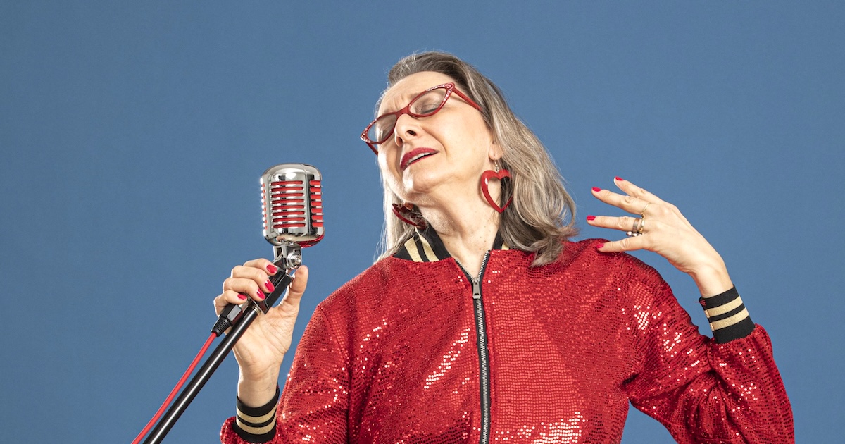 Eine Frau in einer Pailettenjacke singt in ein altertümliches Mikrofon