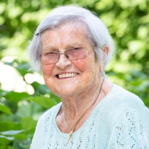 Seniorin vor grüner Gartenkulisse lächelt in die Kamera.