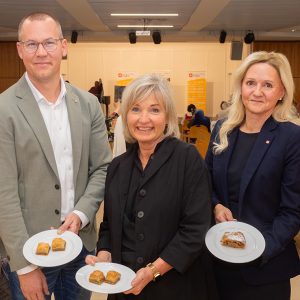 Vertreter*innen der Geschäftsleitung der Häuser zum Leben und politische Ehrengäste halten lächelnd Teller mit Baklava in die Kamera.
