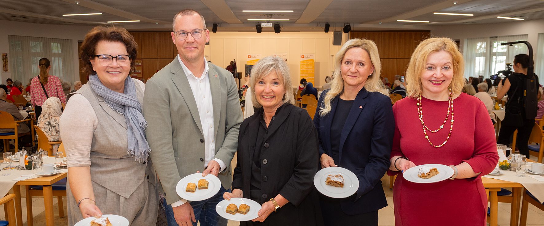 Vertreter*innen der Geschäftsleitung der Häuser zum Leben und politische Ehrengäste halten lächelnd Teller mit Baklava in die Kamera.