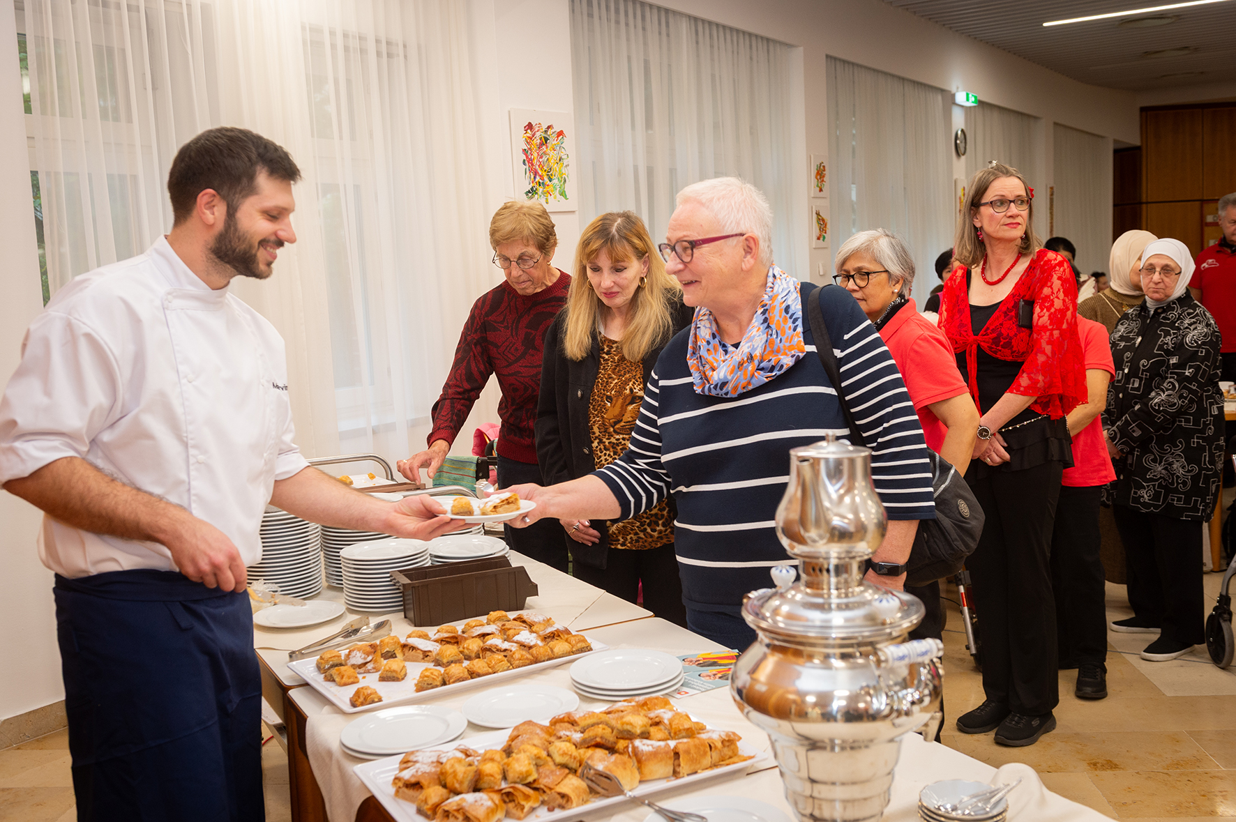 Eine Servicekraft teilt Baklava und Apfelstrudel an Senior*innen aus.