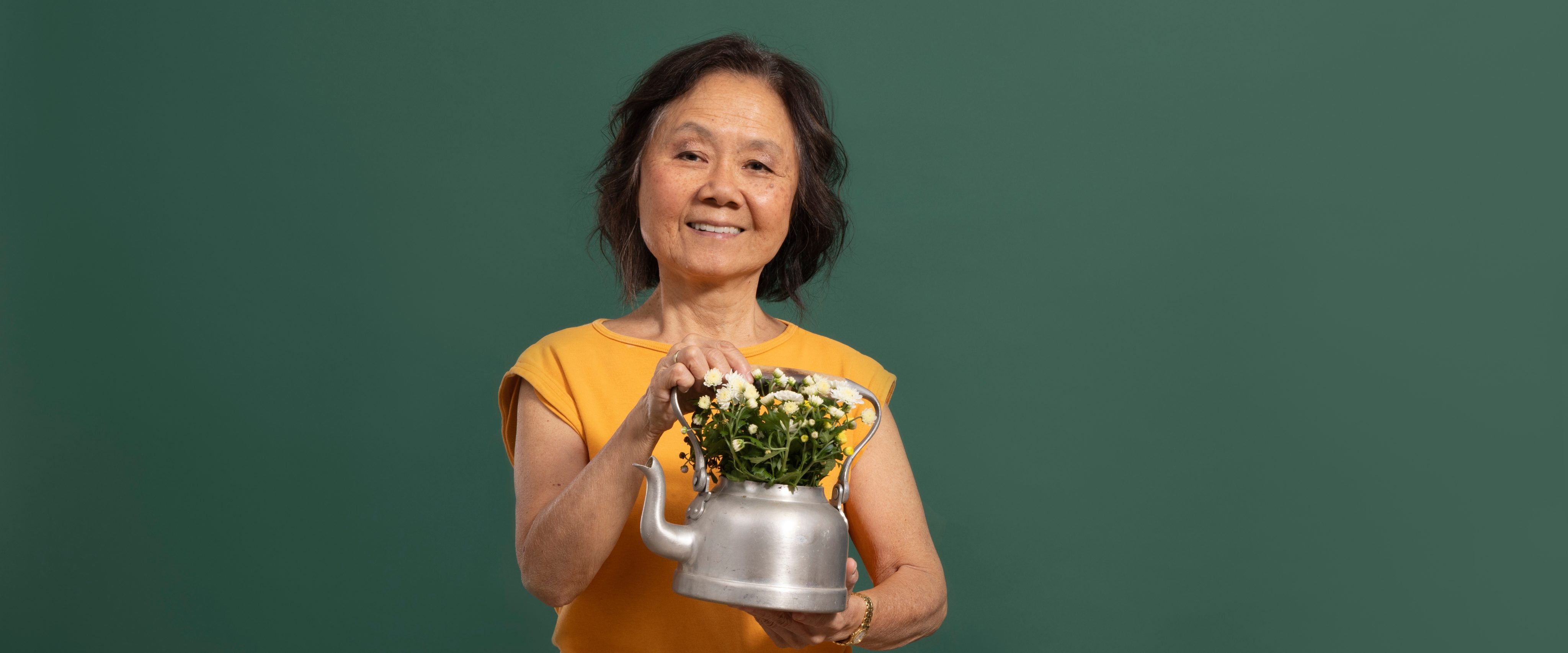 Senior*in hält eine alte Teekanne mit Blumen darin in der Hand.