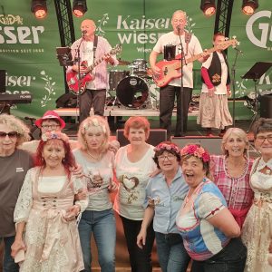 Eine Gruppe Senior*innen posiert vor der Bühne, auf der gerade die Werder Klub Band auftritt.