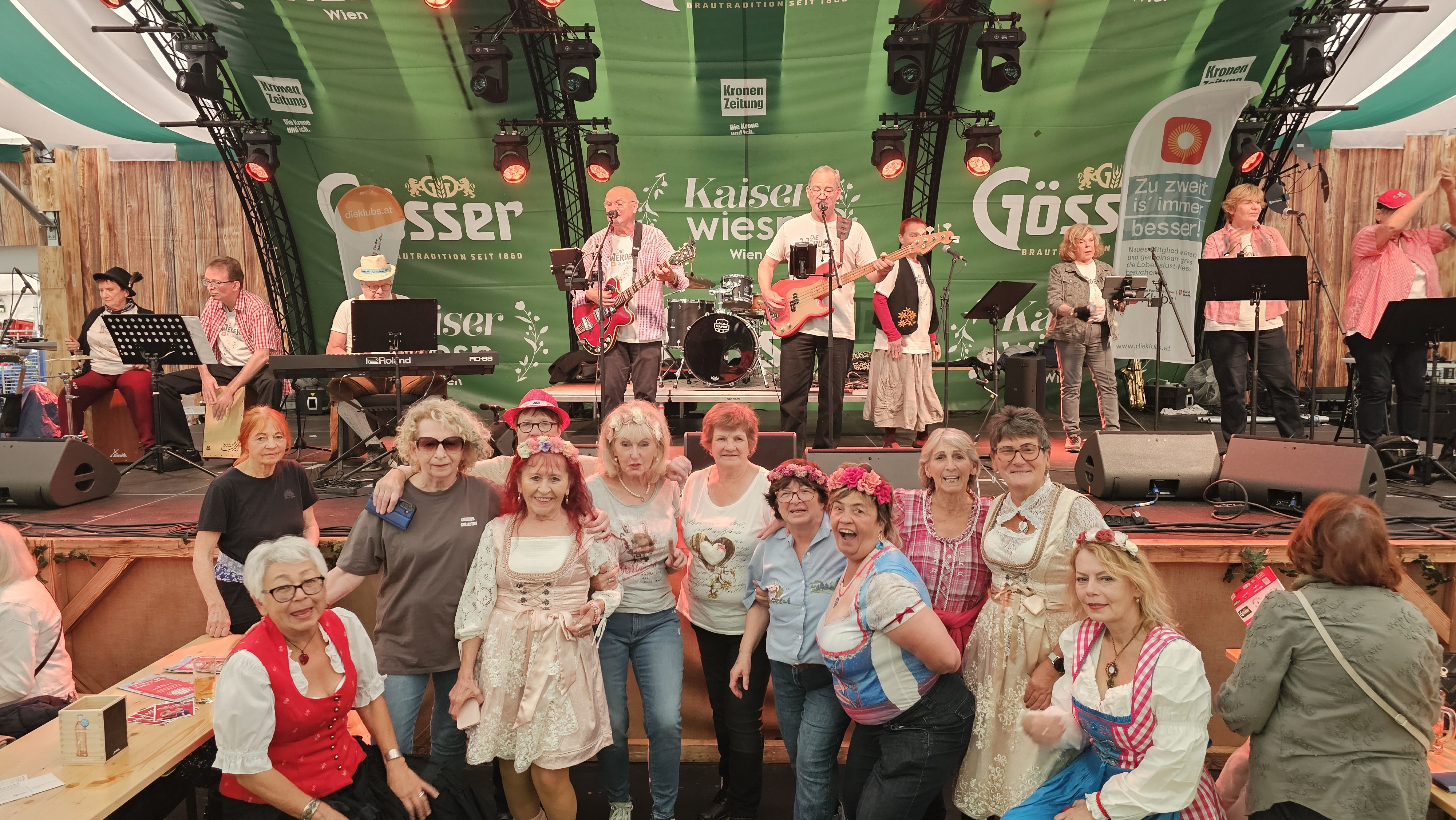 Eine Gruppe Senior*innen posiert vor der Bühne, auf der gerade die Werder Klub Band auftritt.
