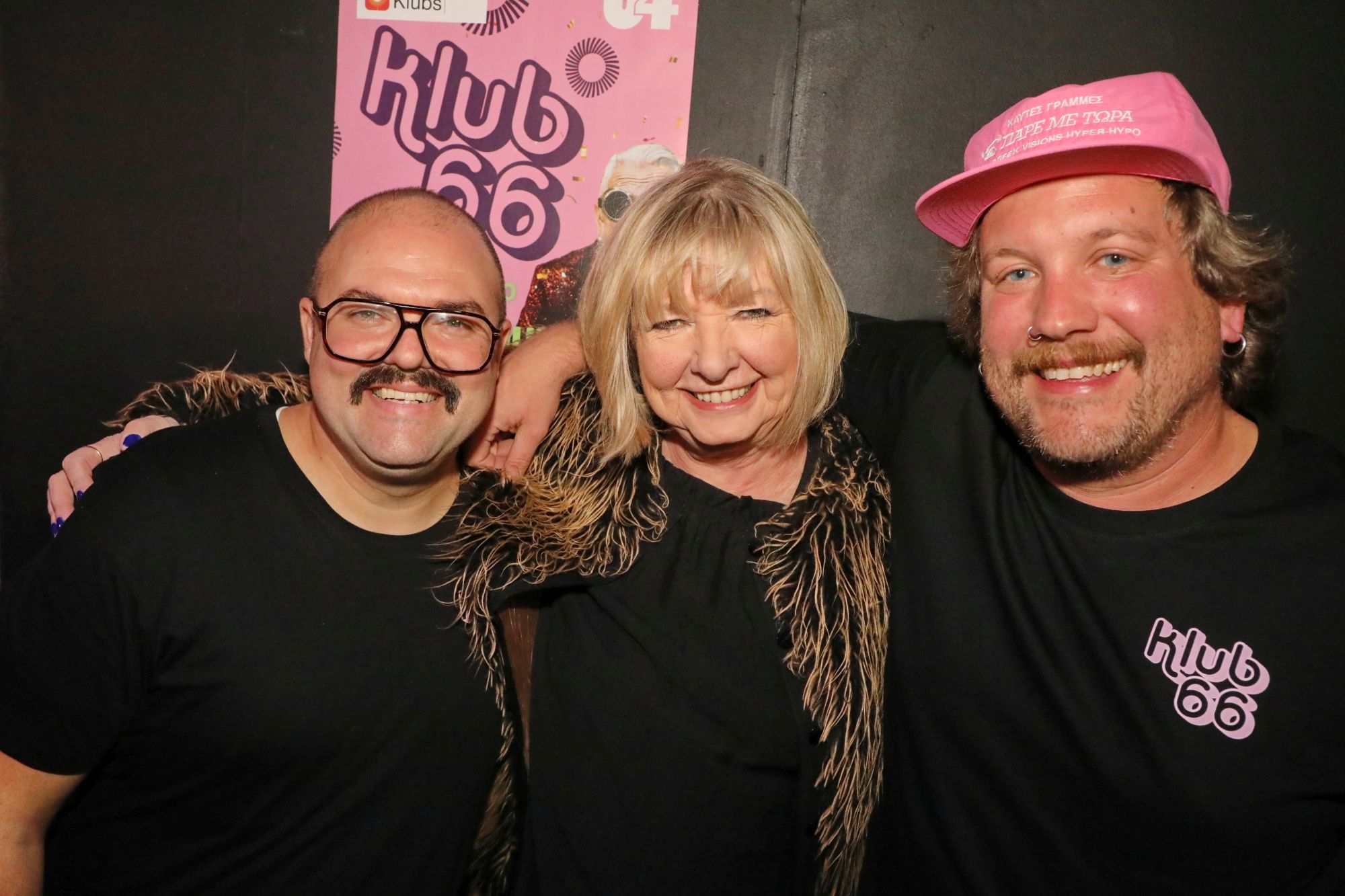 66er Klub im U4 am 06.11.2025 - © Conny de Beauclair zwei junge Männer, einer mit Kappe und der andere mit Brille, posieren Arm in Arm mit einer im Mittelpunkt stehenden Dame für die Kamera