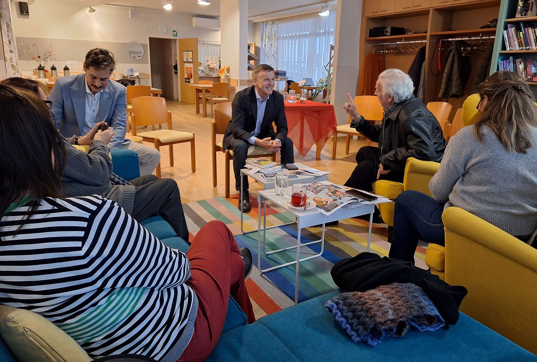 vorlesetag1_taxenbach_gump Eine Runde von Teilnehmer*innen an einer Lesung am Vorlesetag im Pensionist*innenklub Gumpendorfer Straße sitzt auf bequemen Stühlen. In der Mitte der Vorleser: Krimiautor Kornelius Taxenbach.