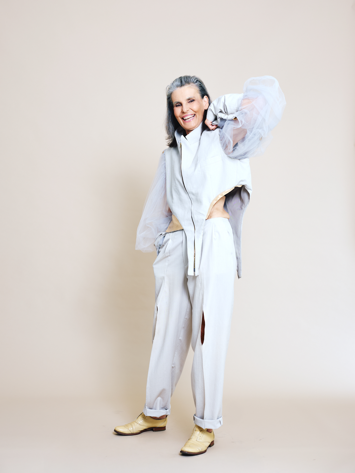 Ein älteres, weibliches Model in ihren selbst entworfenen Gewand (weite, weiße Bluse, weiße Hose) für die Vienna Fashion Week 2026.