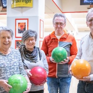 Vier ältere Personen halten Bowlingkugeln in der Hand.