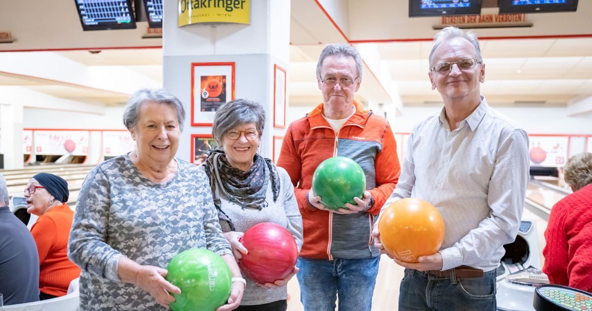 Vier ältere Personen halten Bowlingkugeln in der Hand.