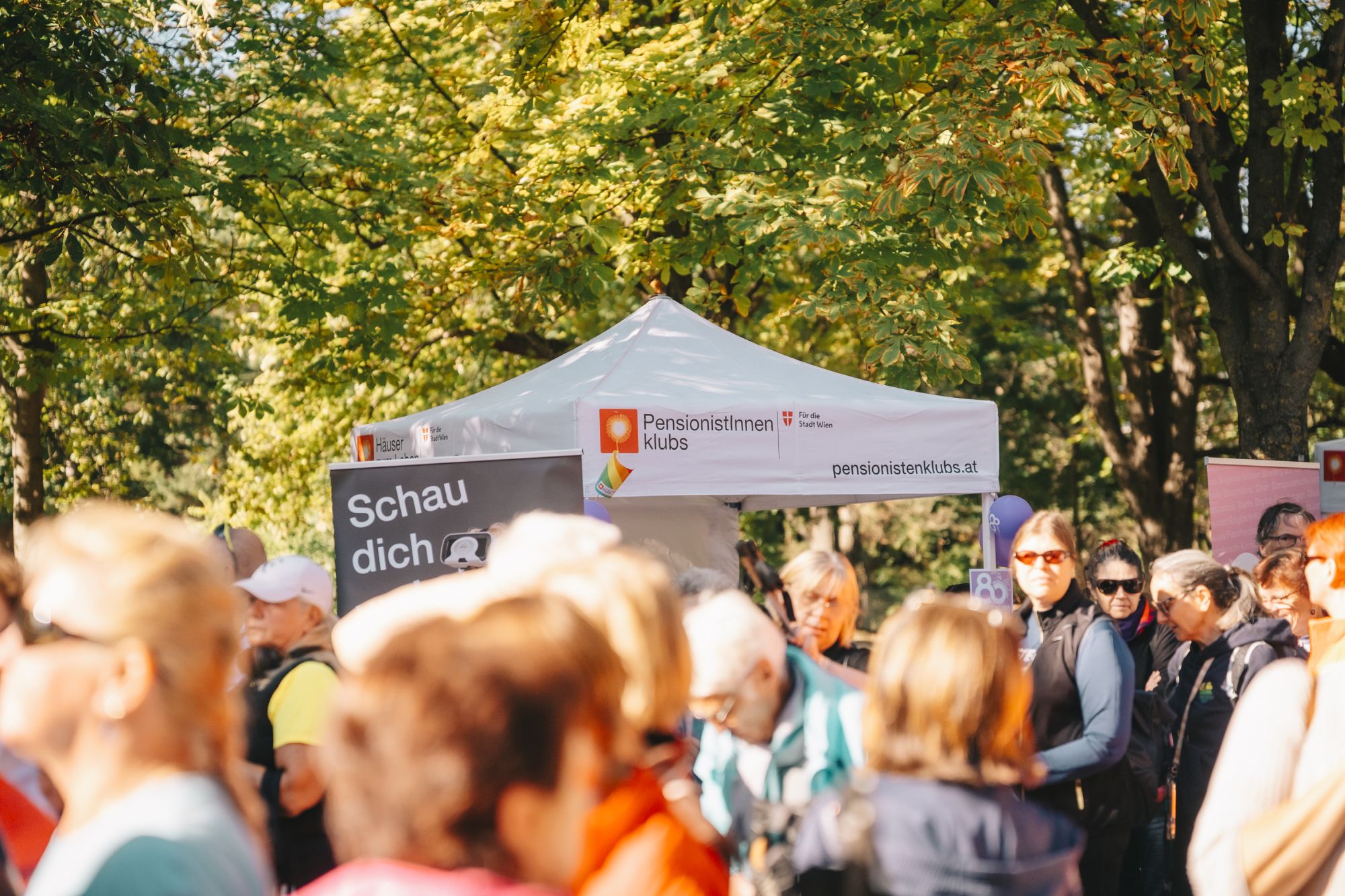SENWDAY_(c)_David_Bohmann_035 Mehrere Teilnehmer*innen beim Nordic Walking Day 2026 (großteils von hinten) vor einem Zelt mit der Aufschrift "Pensionist*innenklubs".