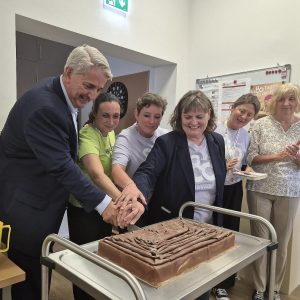 Ernst Nevrivy, Bezirksvorsteher Donaustadt, und andere Personen schneiden eine Torte anlässlich der Wiedereröffnung des Pensionist*innenklubs Rennbahnweg an.