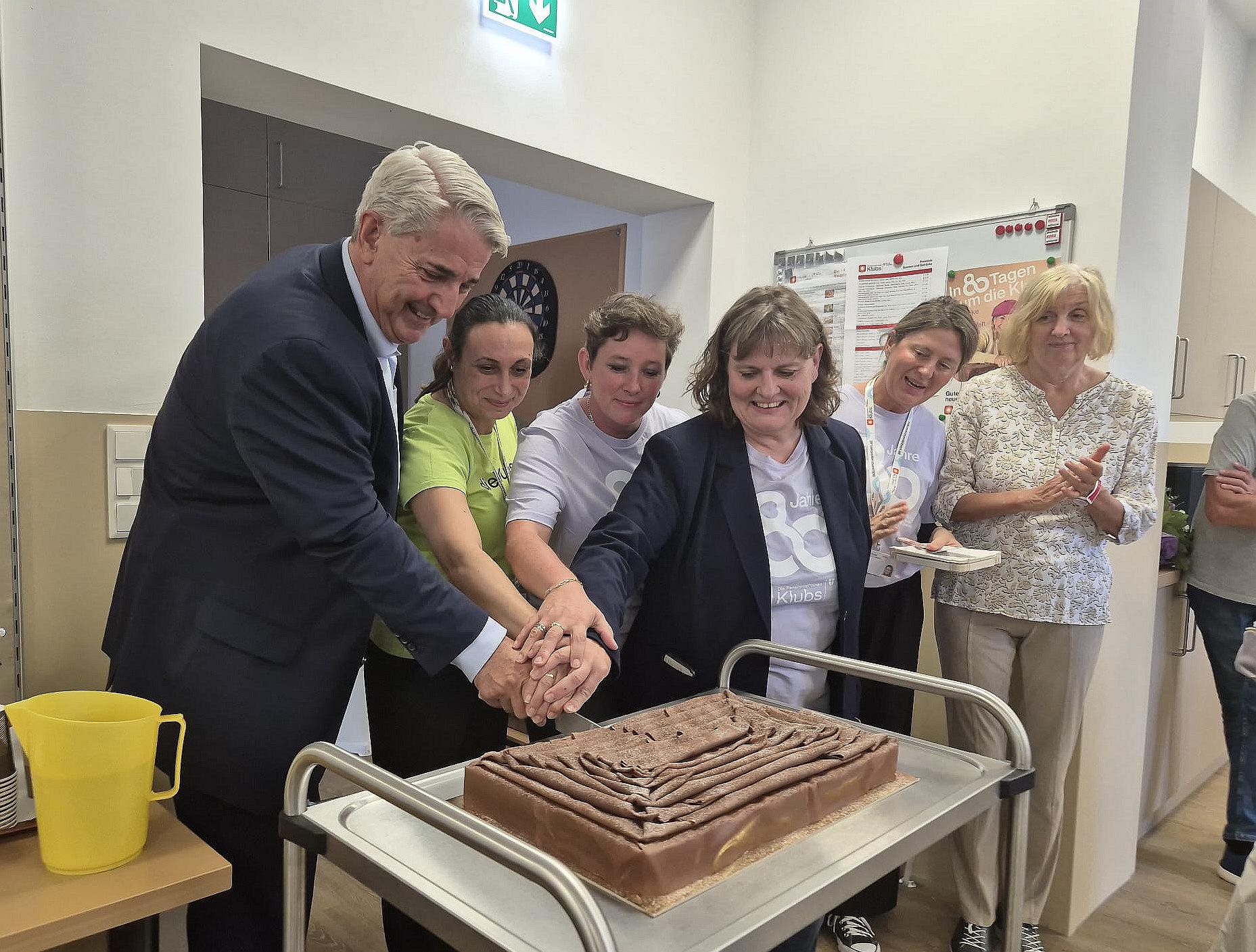 Ernst Nevrivy, Bezirksvorsteher Donaustadt, und andere Personen schneiden eine Torte anlässlich der Wiedereröffnung des Pensionist*innenklubs Rennbahnweg an.