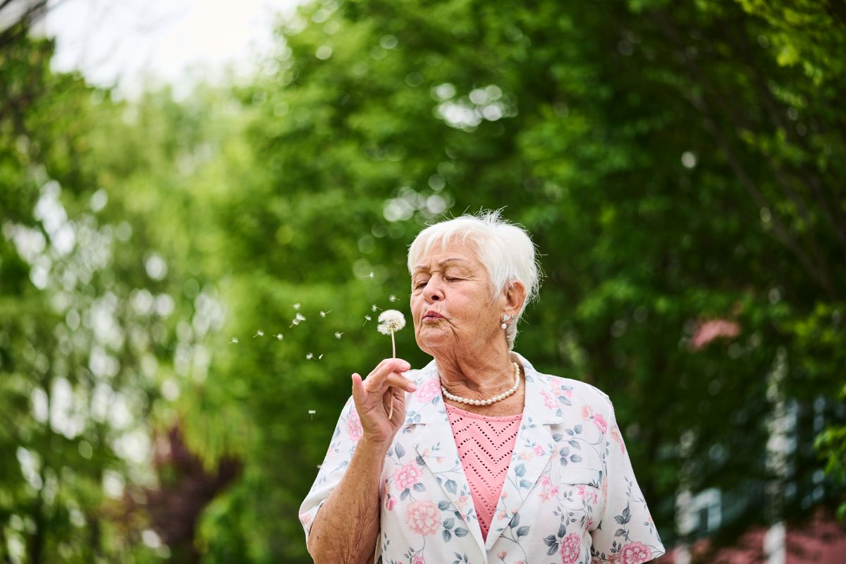 Eine Seniorin pustet an einer Pusteblume.