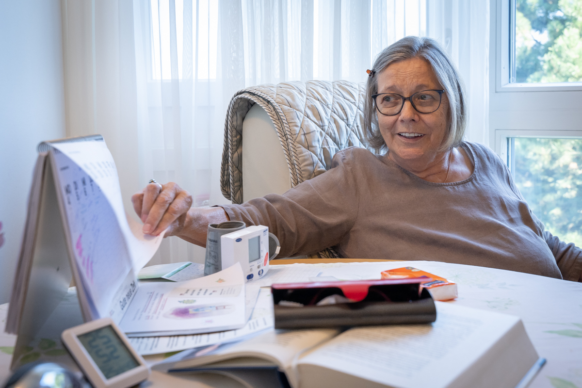 Eine ältere Frau mit Pagenkopf und Brille blättert an einem Tischkalender.