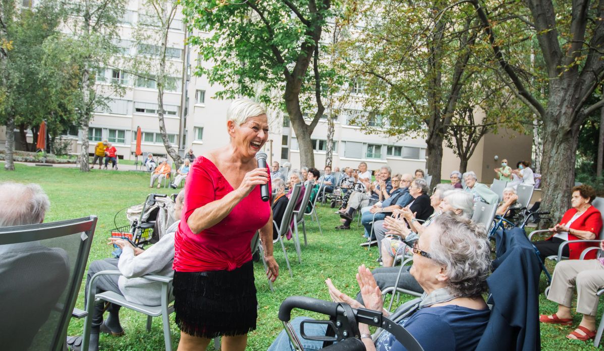 Die Sängerin Jazz Gitti singt im Garten vor älteren Menschen.