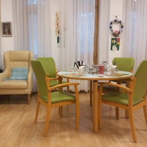 Ein Tisch mit vier hellgrünen Stühlen und ein beiges Fauteuil stehen in einem hellen Raum.