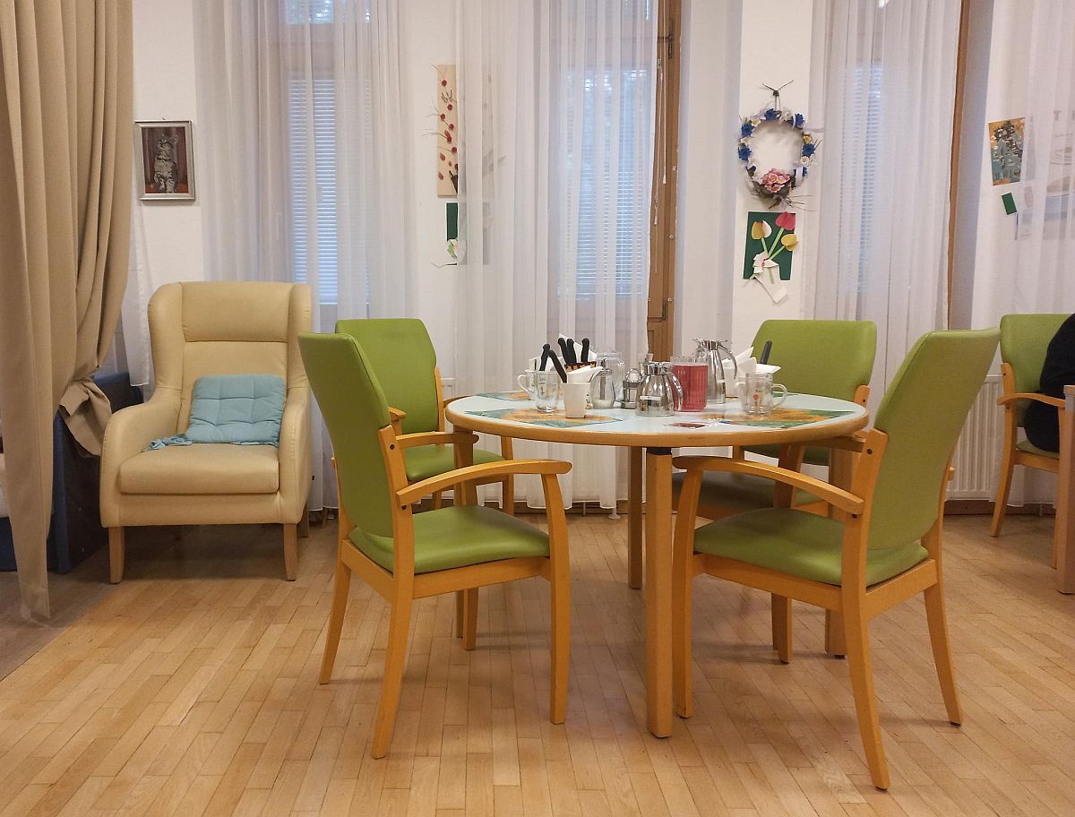 Ein Tisch mit vier hellgrünen Stühlen und ein beiges Fauteuil stehen in einem hellen Raum.