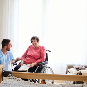 Pflegekraft spricht mit älteren Frau, die im Rollstuhl sitzt