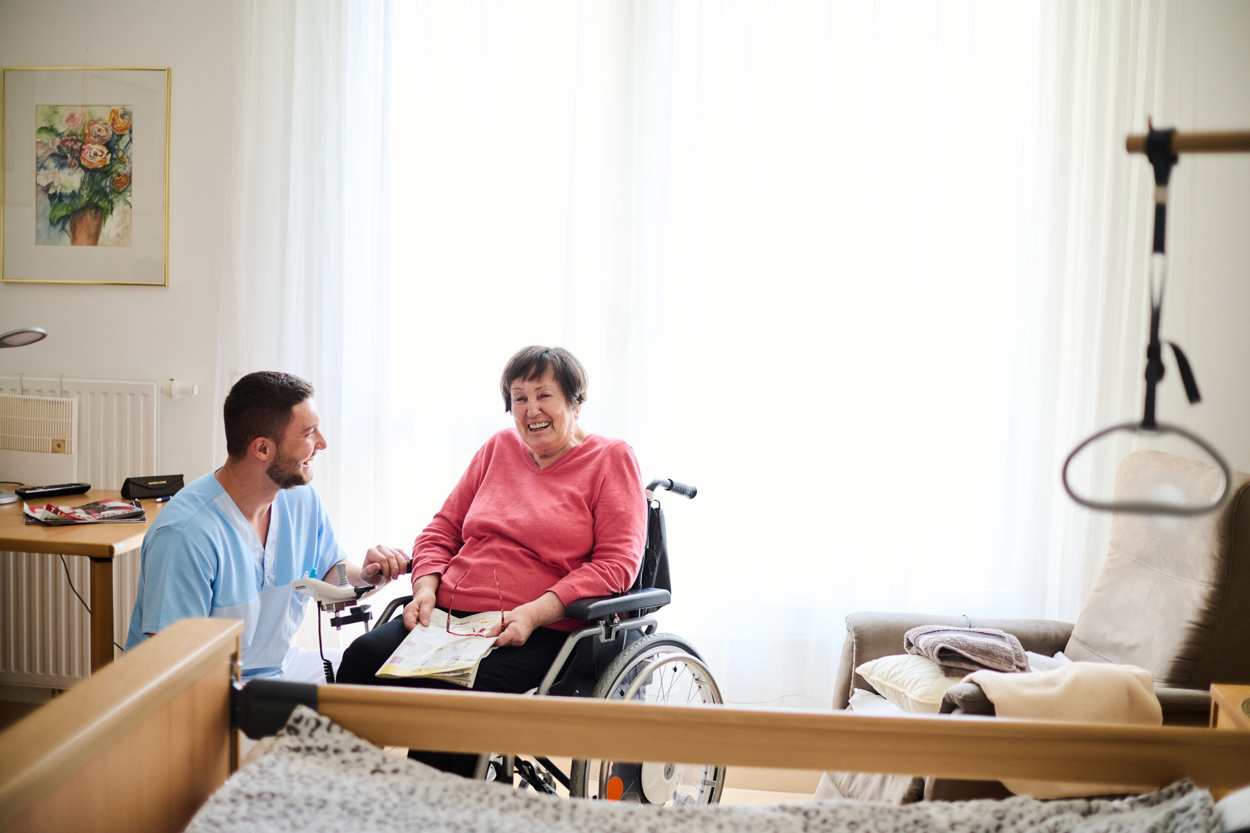 Pflegekraft spricht mit älteren Frau, die im Rollstuhl sitzt
