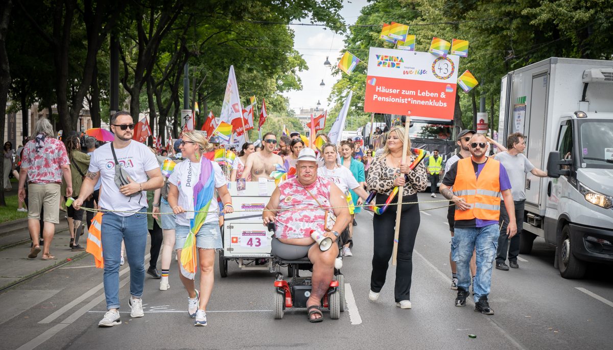 Personen mit einem Schild "Häuser zum Leben, Pensionist*innenklubs" auf der Regenbogenparade