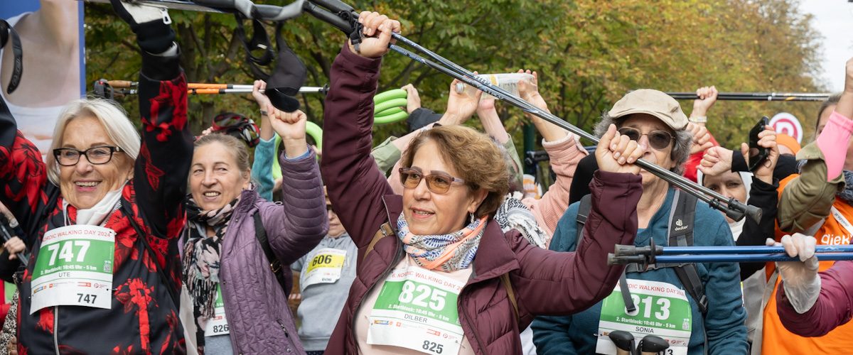 Teilnehmer*innen des Senior*innen Nordic Walking Day halten an der Startlinie ihre Walking-Stöcke in die Höhe.