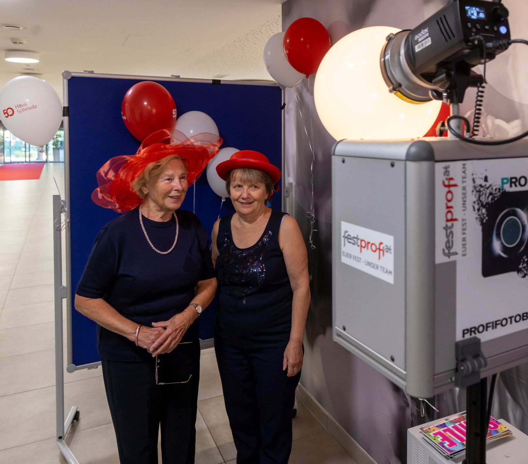 Zwei Frauen mit roten Hüten stehen hinter einer Fotobox.
