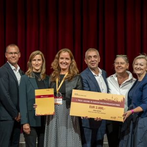 Gruppenbild mit u.a. Stadtrat Peter Hacker, Simon Bluma (stv. Geschäftsführer Häuser zum Leben), Viktoria Holler (Regionalleiterin Häuser zum Leben), Ulrike Geier-Palaschke (Direktorin Haus Liebhartstal) mit einer Urkunde und einem Preisscheck über 2000 Euro für den Gewinn beim WiG-Gesundheitspreis.