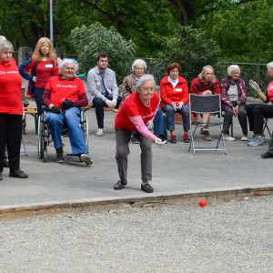 Eine Frau wirft eine Boccia-Kugel, mehrere Personen im Hintergrund schauen zu.