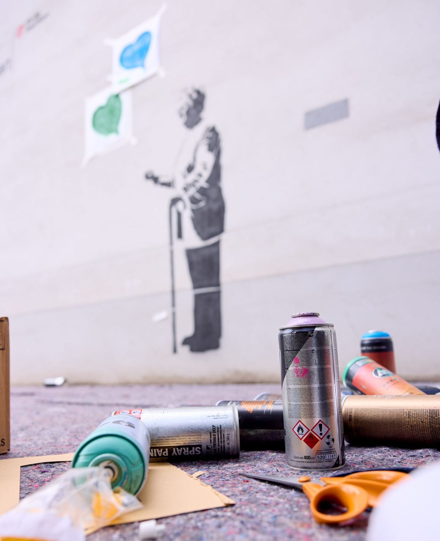 Spraydosen im Vordergrund, im Hintergrund eine an die Wand gesprayte Seniorin