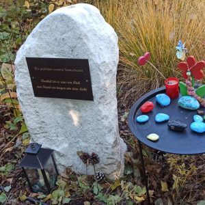 Ein Gedenkstein und ein Tisch mit kleinen, bunten Steinen und Kerzen im Garten des Hauses Schmelz.