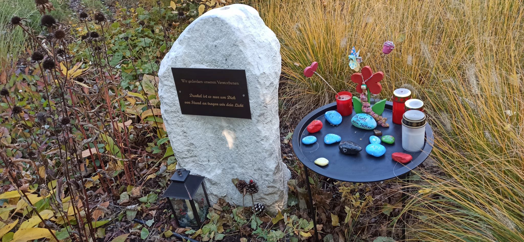 Ein Gedenkstein und ein Tisch mit kleinen, bunten Steinen und Kerzen im Garten des Hauses Schmelz.