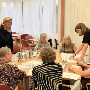 An einem Tisch sitzen Bewohner*innen-Beiräte und Mitarbeiter*innen der Häuser zum Leben im Rahmen eines Workshops.