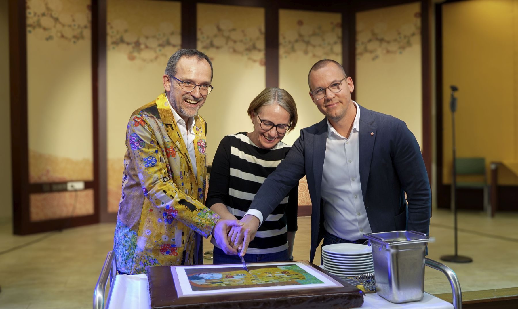 Gerhard Schlachter, Direktor Haus Gustav Klimt, Michaela Schüchner, Bezirksvorsteherin Penzing, Simon Bluma, stellvertretender Geschäftsführer Häuser zum Leben, schneiden eine Geburtstagstorte an.