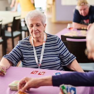 Eine Seniorin und ein Senior spielen miteinander Karten an einem Tisch.