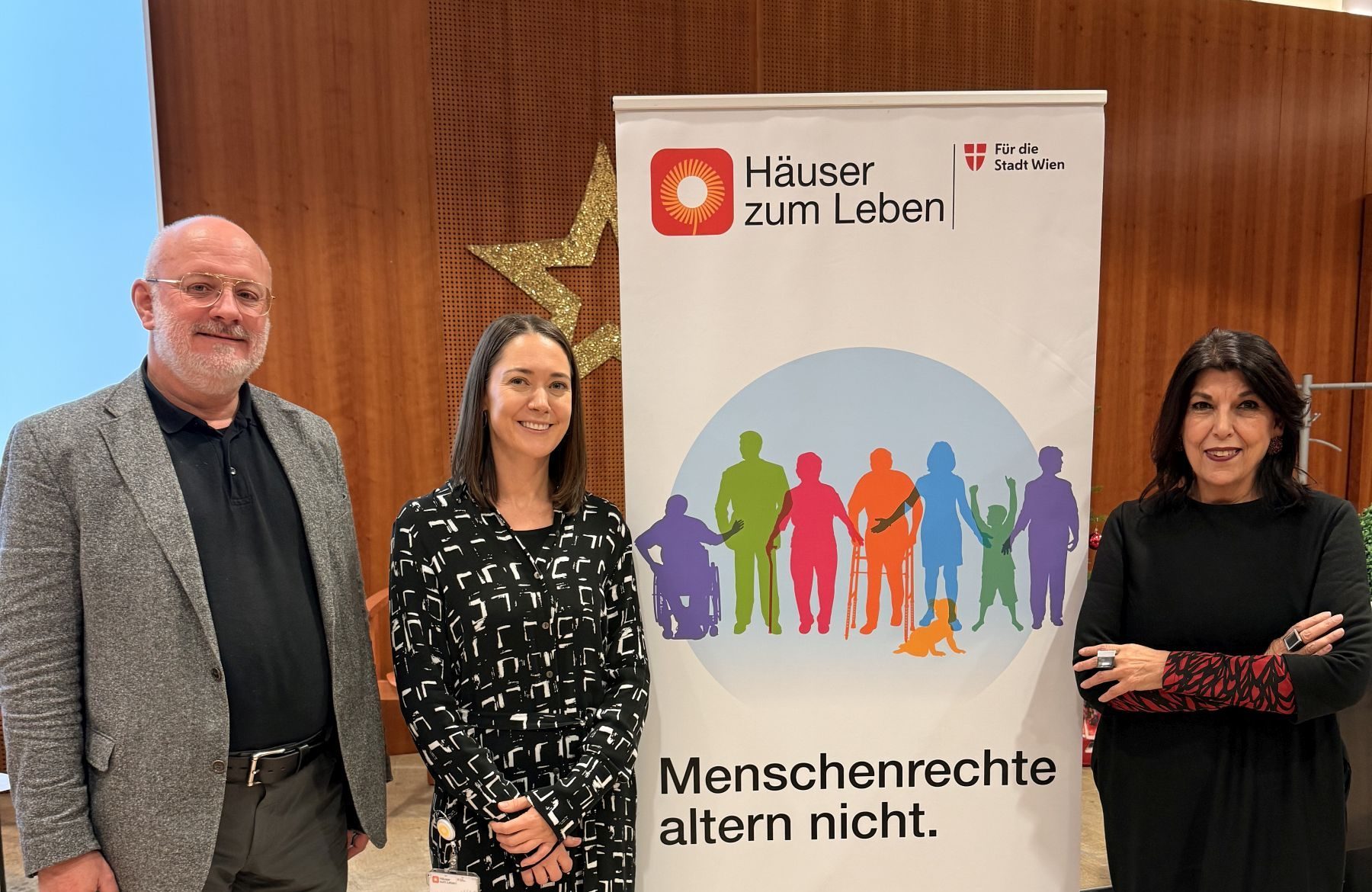 Heinz Stieb, Bereichsleiter Pflege und Betreuung Häuser zum Leben, Gudrun Bauer, Leiterin Stabsstelle Strategie und Entwicklung Häuser zum Leben, Shams Asadi, Menschenrechtsbeauftragte der Stadt Wien stehen neben einem Roll-up mit der Aufschrift "Menschenrechte altern nicht".