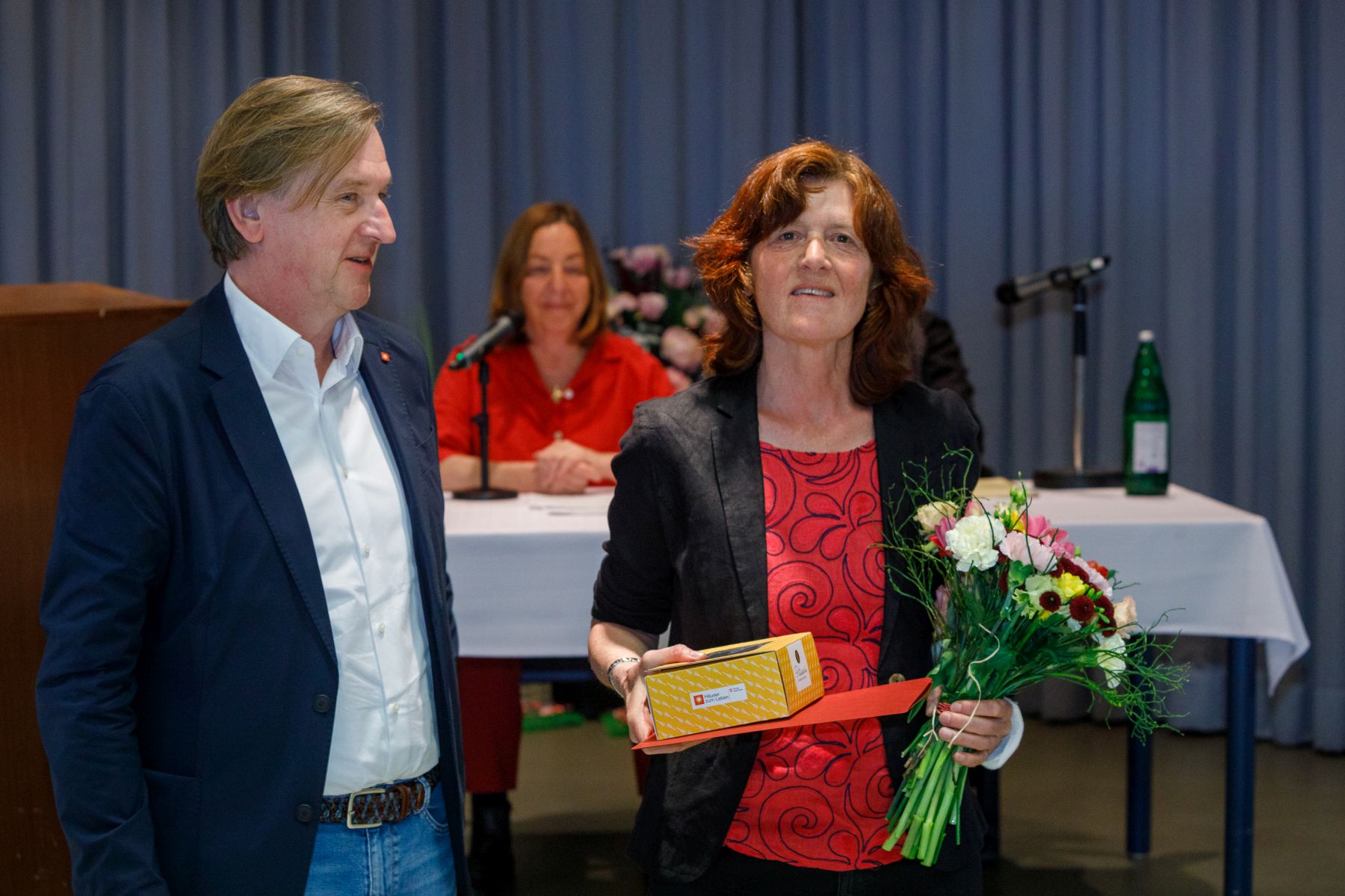 Christian Hennefeind, Geschäftsführer Häuser zum Leben steht neben Gewinnerin Karin Leroch. Im Hintergrund sitzt die Schauspielerin Susi Stach.