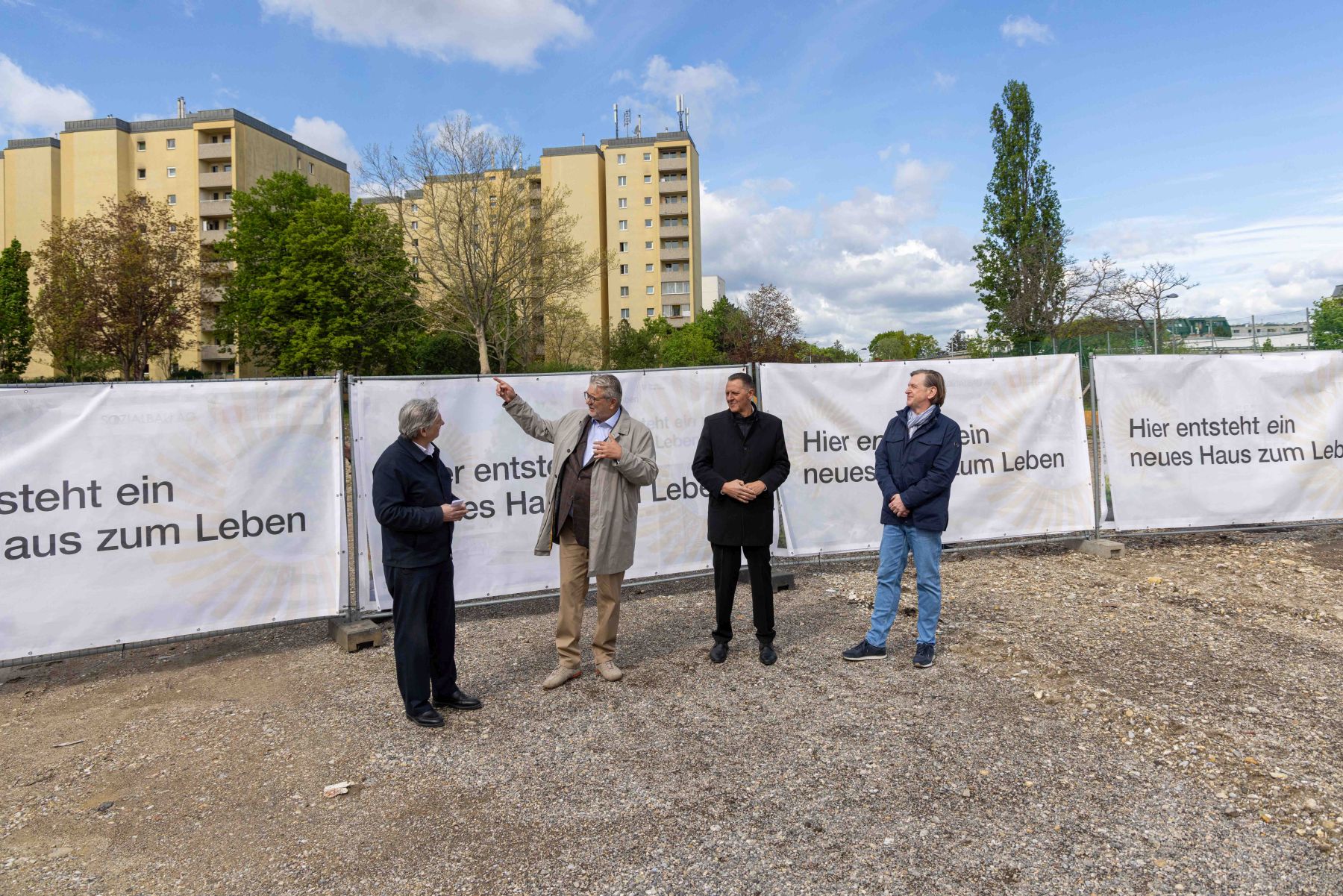 Sozialstadtrat Peter Hacker steht mit anderen Männern vor Bauzaunplanen mit der Aufschrift "Hier entsteht ein neues Haus zum Leben".