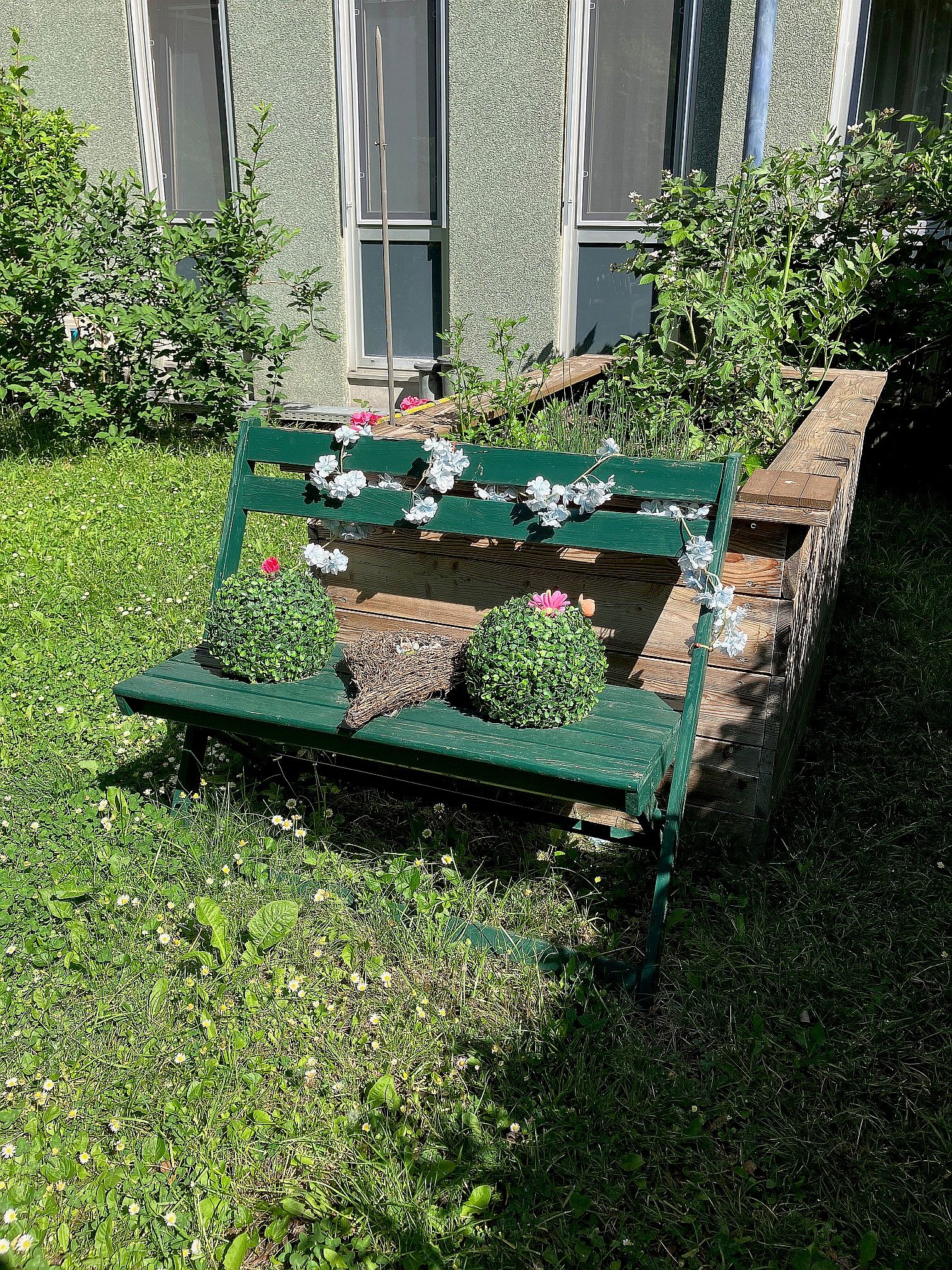 bank Eine grüne Gartenbank steht vor einem Hochbeet in der Wiese im Garten des Pensionisten-Wohnhauses Prater.