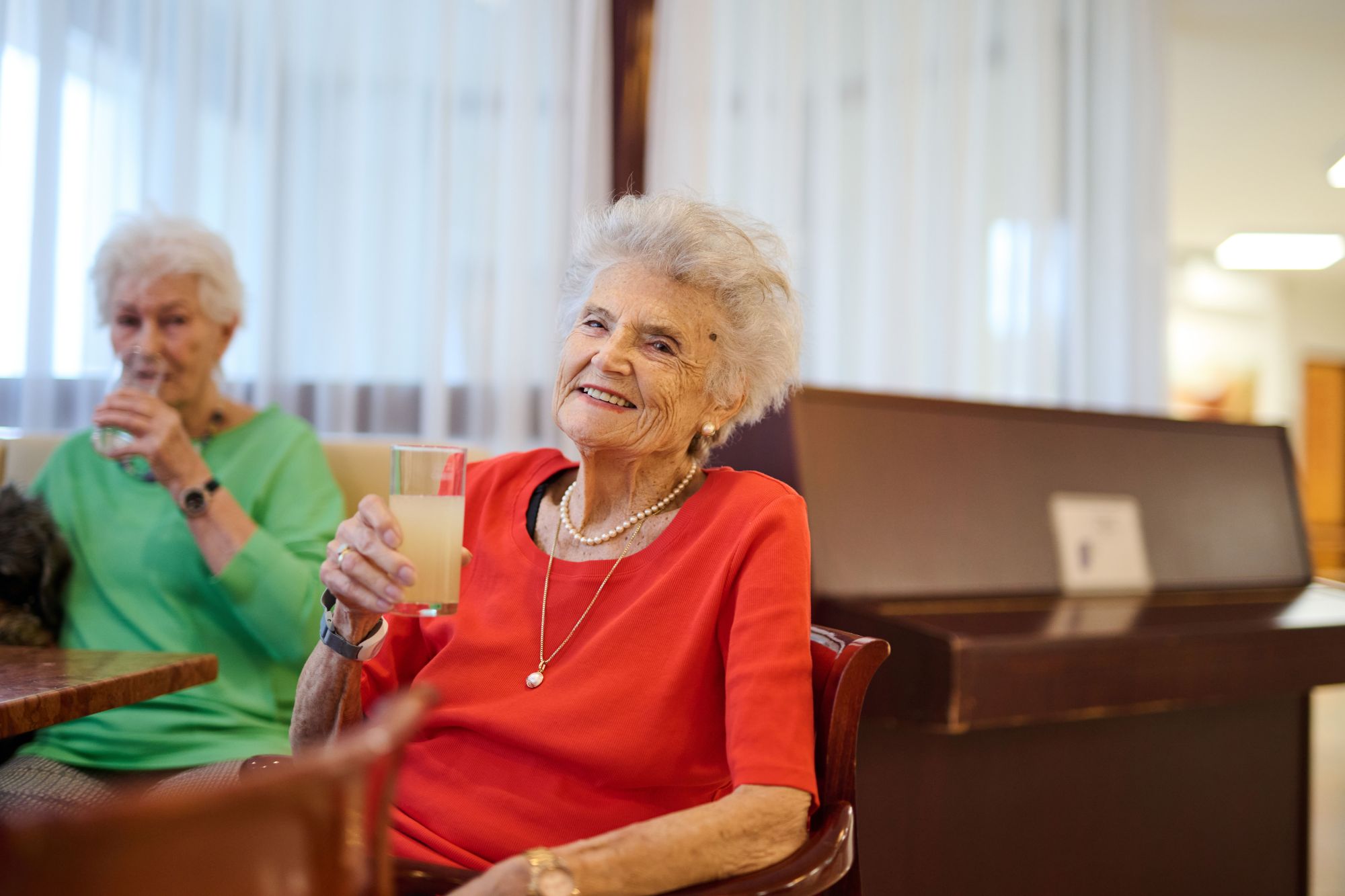 Zwei Seniorinnen halt ein Glas mit einem Getränk in der Hand.