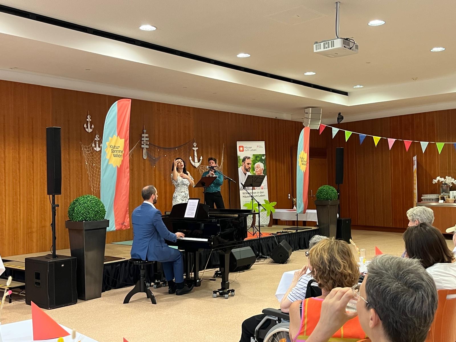 Eine Sängerin und ein Musiker auf einer Bühne und ein Klavierspieler vor der Bühne.