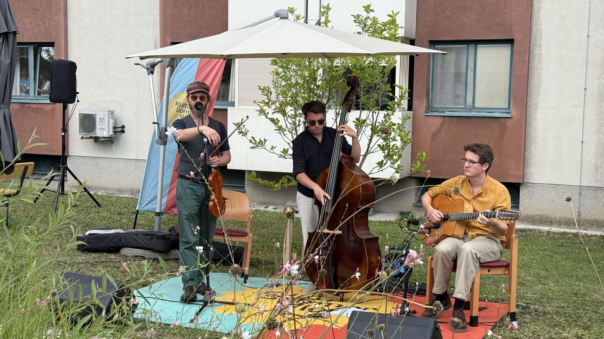 Drei Musiker mit Geige, Kontrabass und Gitarre auf der Bühne im Garten des Hauses Alszeile.