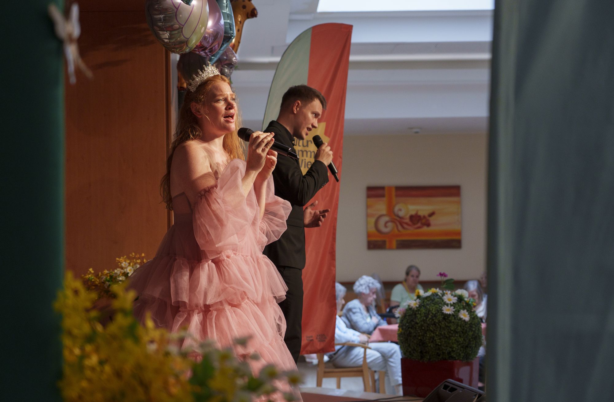 Eine Sängerin in einem pompösen rosa Kleid und ein Sänger in schwarz auf der Bühne im Haus Mariahilf.