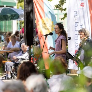Eine Sängerin und ein Geiger auf einer Bühne im Garten des Hauses Hohe Warte beim Gartenkonzert im Rahmen von Kultursommer Wien.