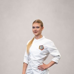 Koch-Lehrling Anastasia posiert in Kochjacke und schwarzer Hose.