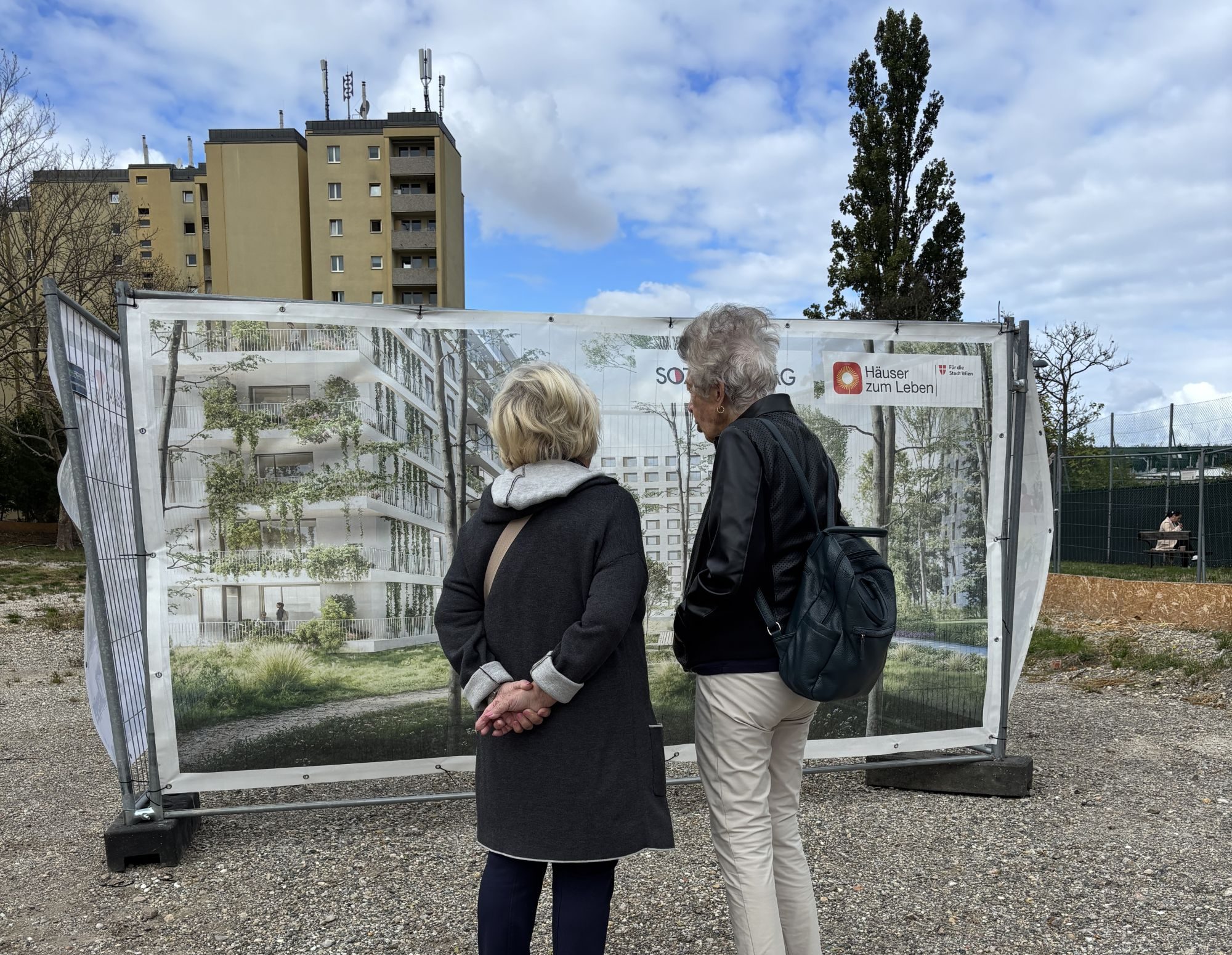 Zwei Frauen (von hinten) betrachten eine Plane, auf der ein Rendering des neuen Hauses Haidehof zu sehen ist.